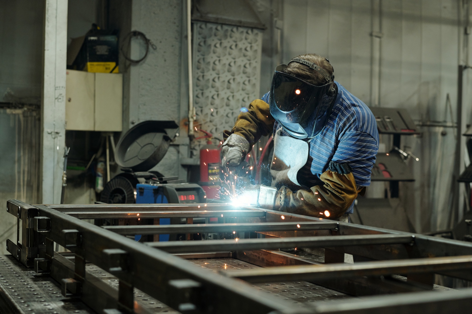 Young male welder in protective mask and gloves welding metallic structure